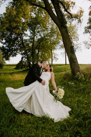 Romantic wedding couple twirls in a flowing white dress against natural outdoor backdrop.
