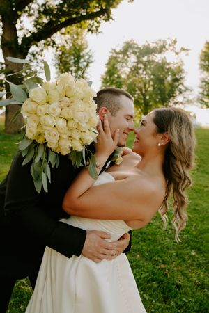 Couple shares romantic moment with white rose bouquet in outdoor garden setting.
