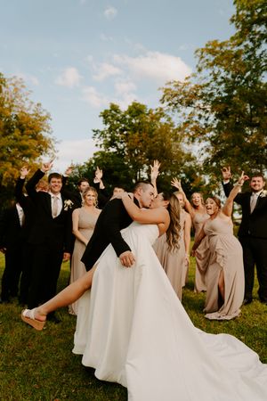 Wedding party celebrates with raised arms and joyful expressions in outdoor setting.