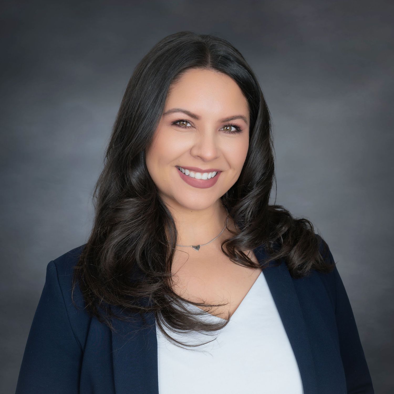 Professional healthcare worker in navy blue scrubs poses for portrait against gray background.