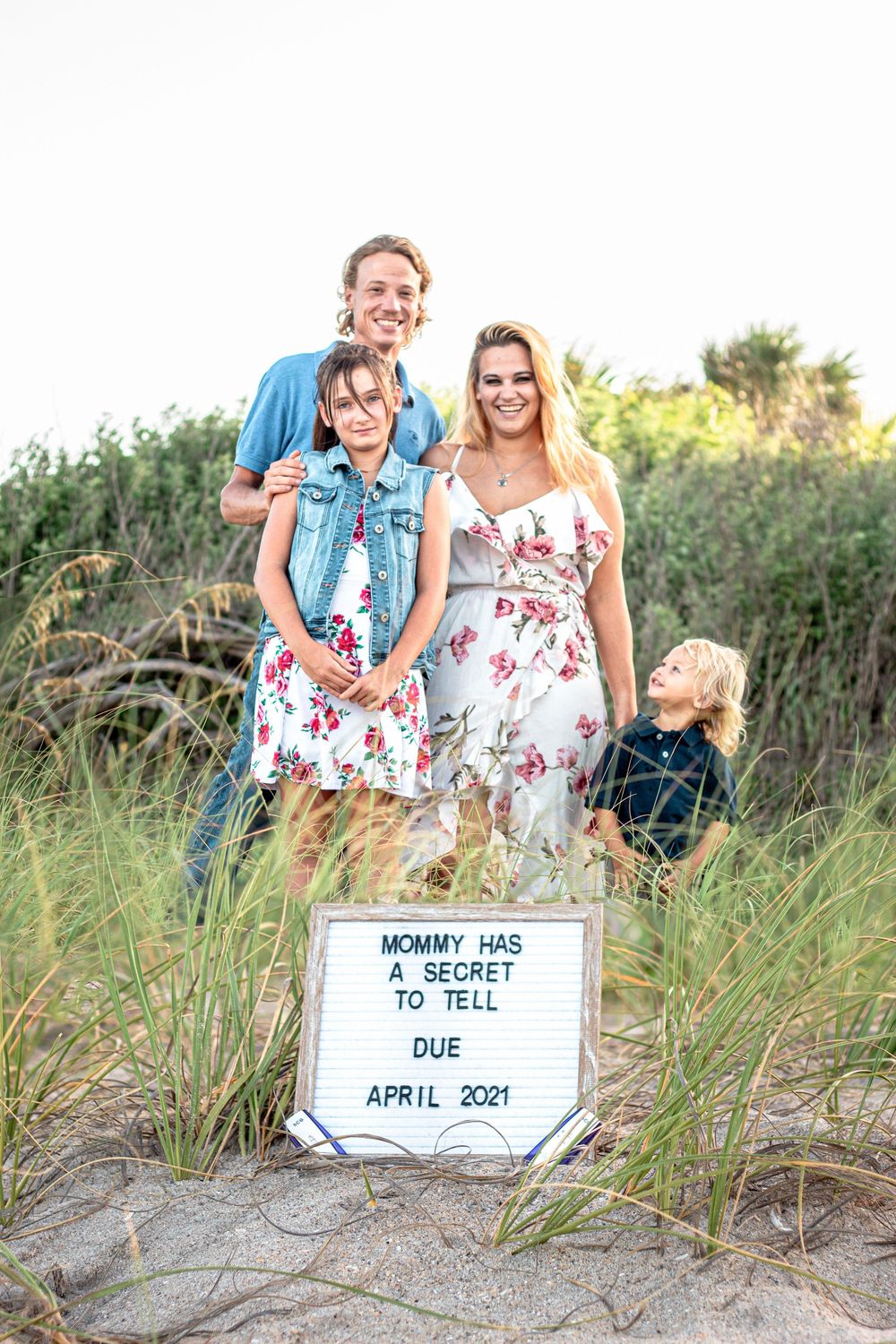 Family photo on lake worth beach with sign announcing pregnancy due in April 2021.