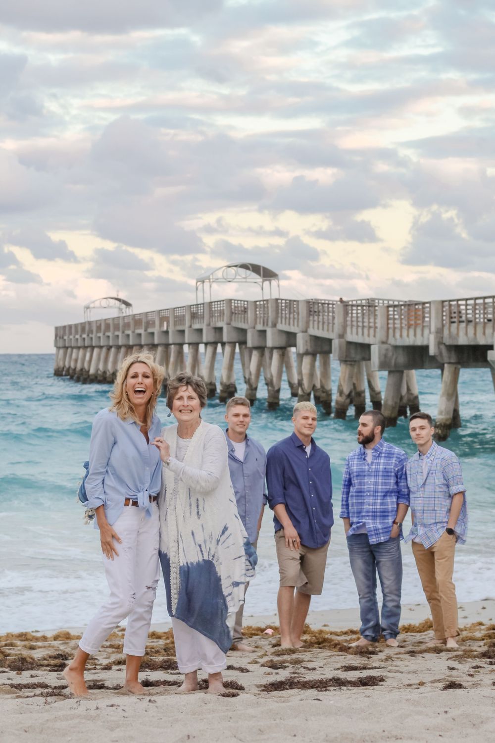 A family group poses on a beach at sunset with a wooden pier in the background at lake worth beach Florida