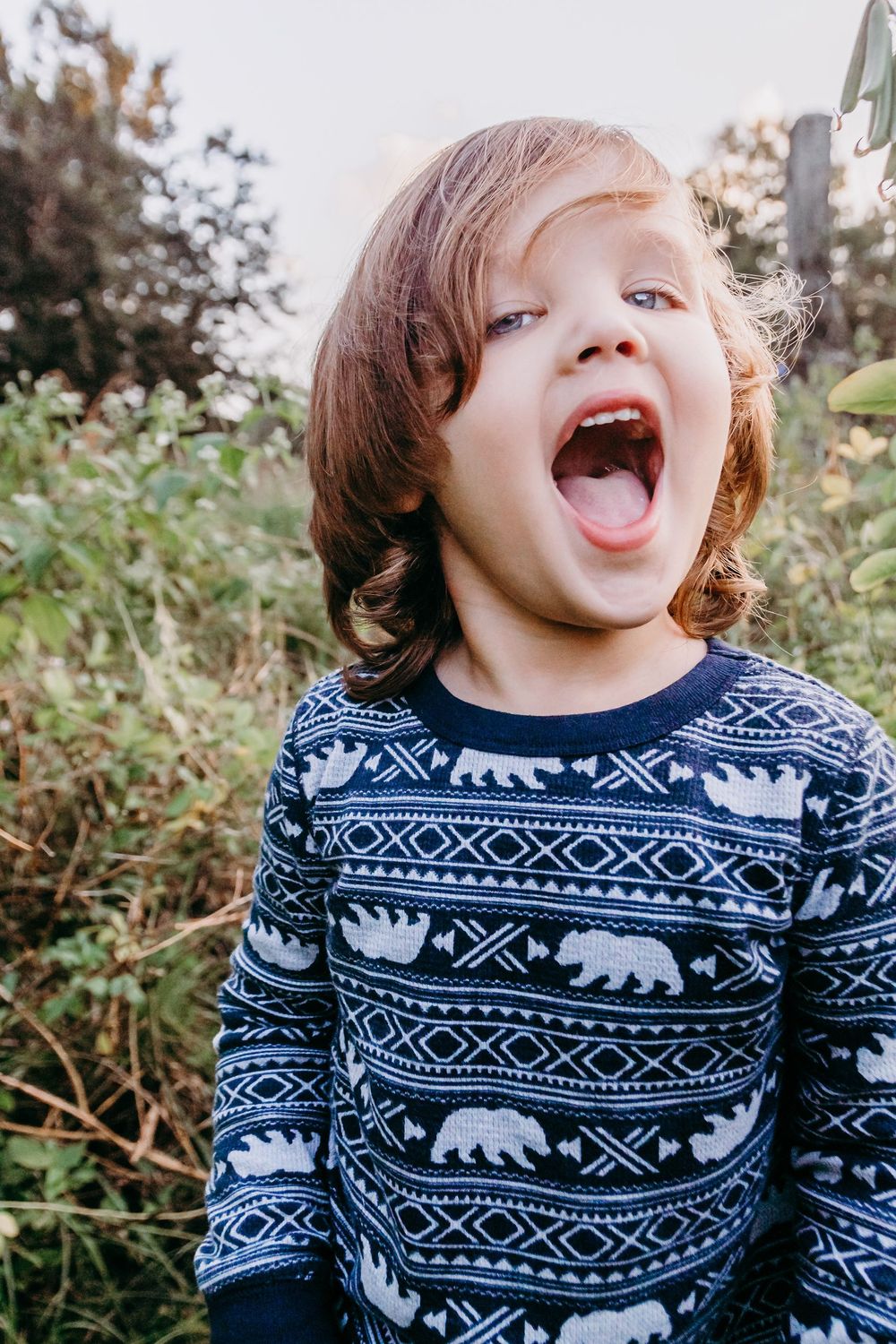 A child wearing a blue sweater with polar bear pattern laughing joyfully outdoors at Riverbend park Jupiter