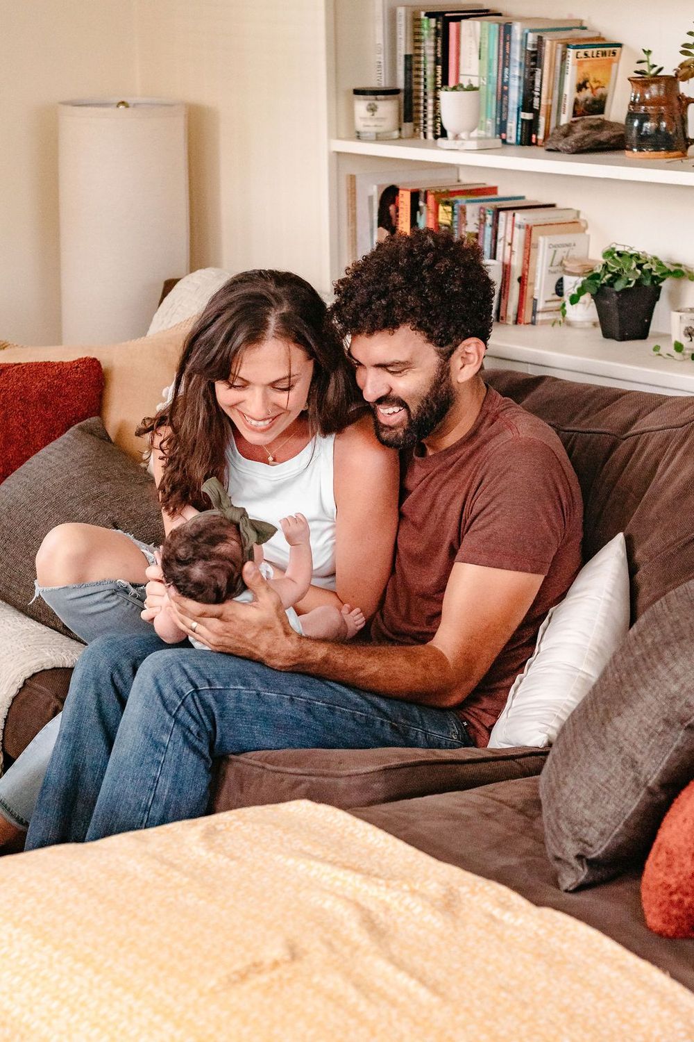 Couple relaxing on brown couch with newborn baby in cozy living room setting.