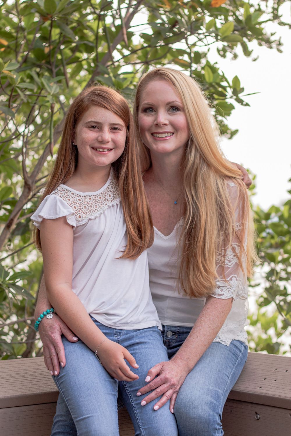 Casual outdoor portrait of mother and daughter sitting together near foliage in Boca Raton, red reef park