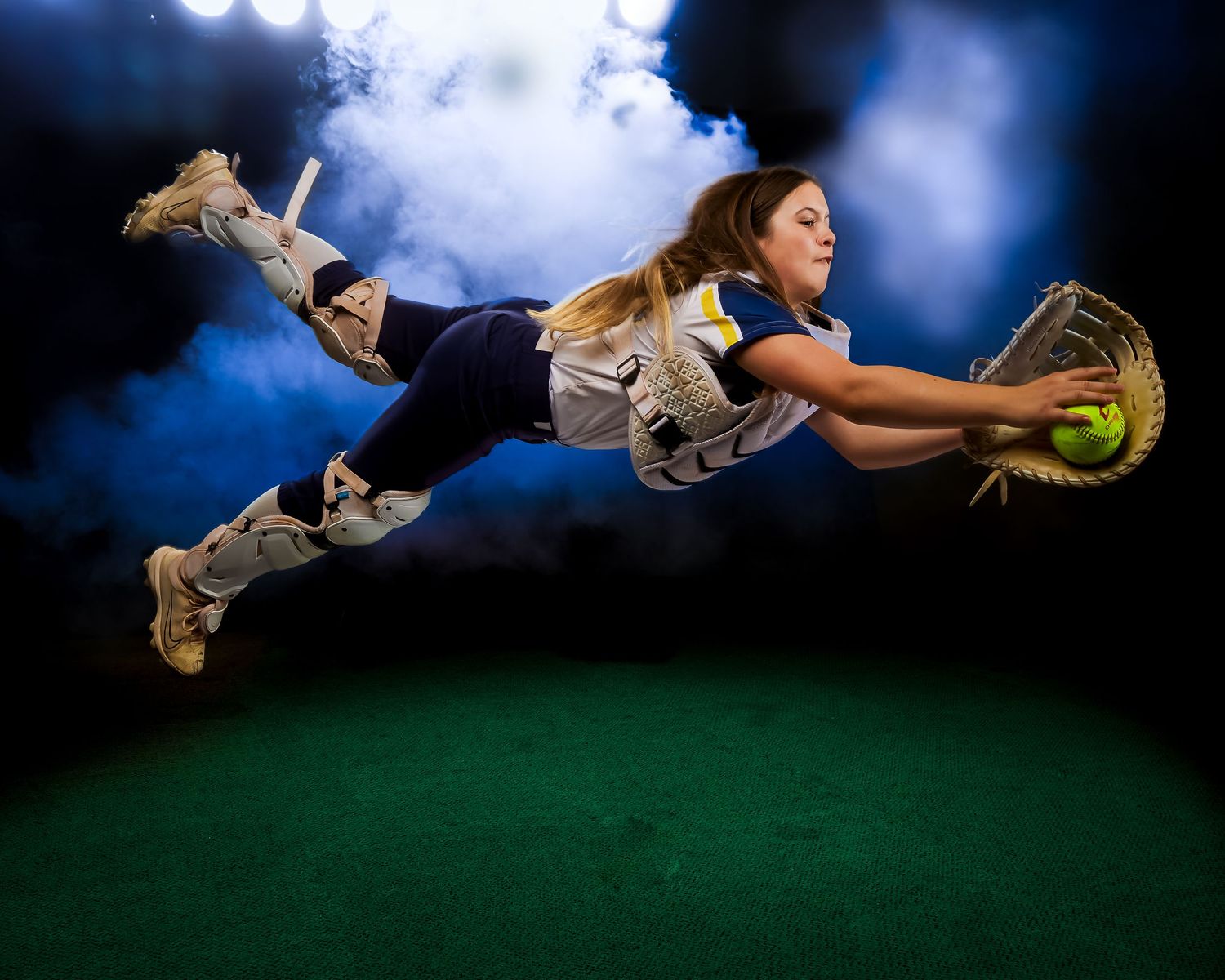 Softball player diving horizontally in mid-air to catch a ball against a dramatic blue and green backdrop.