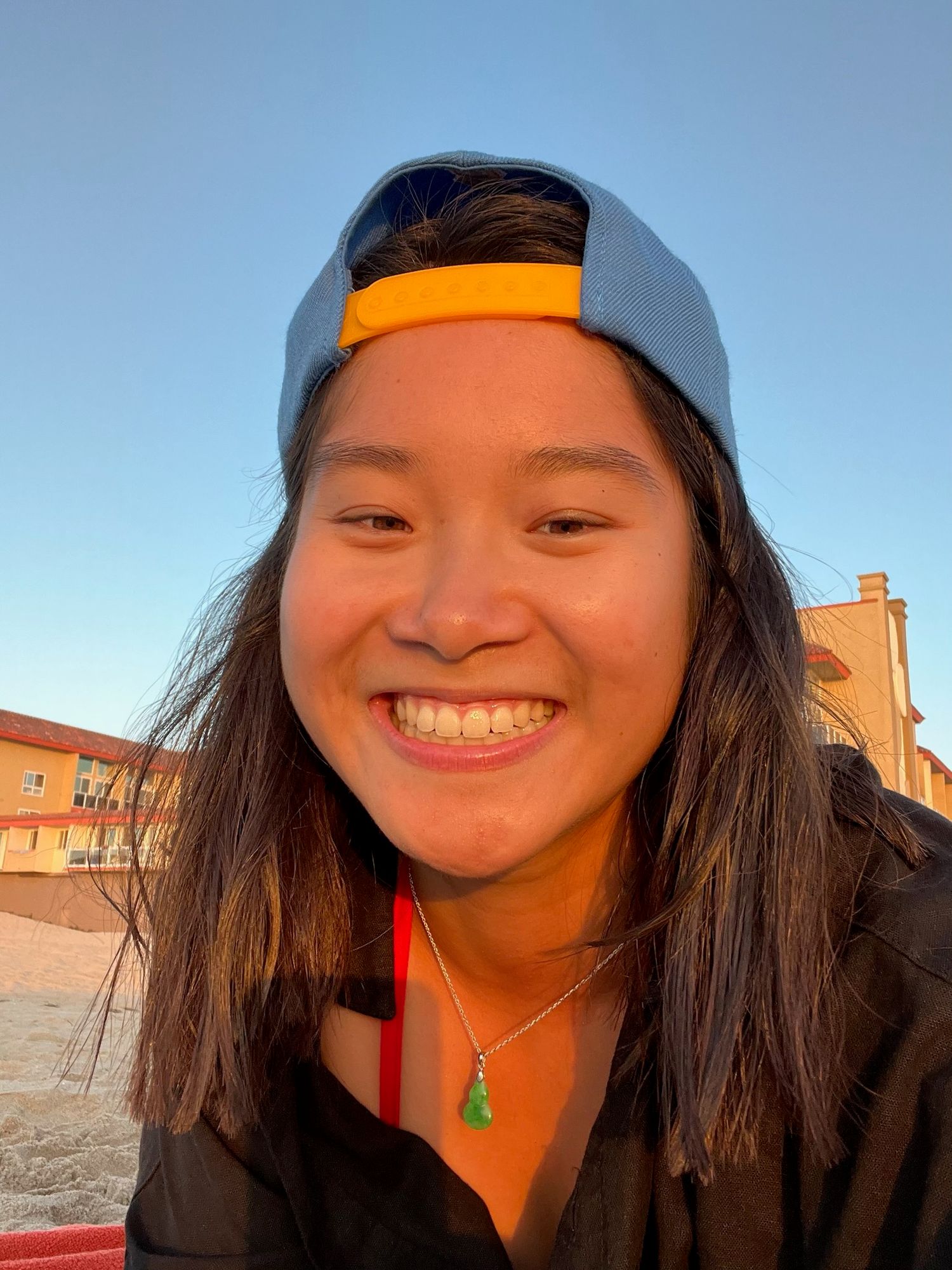 Person wearing baseball cap smiling outdoors in sunset light.