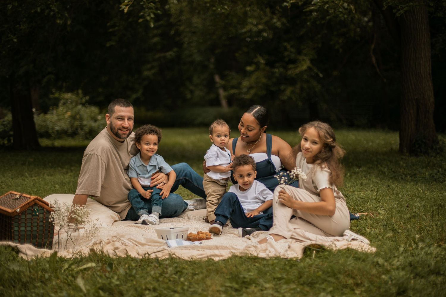 A family of six poses together against a stone wall surrounded by greenery at dusk.