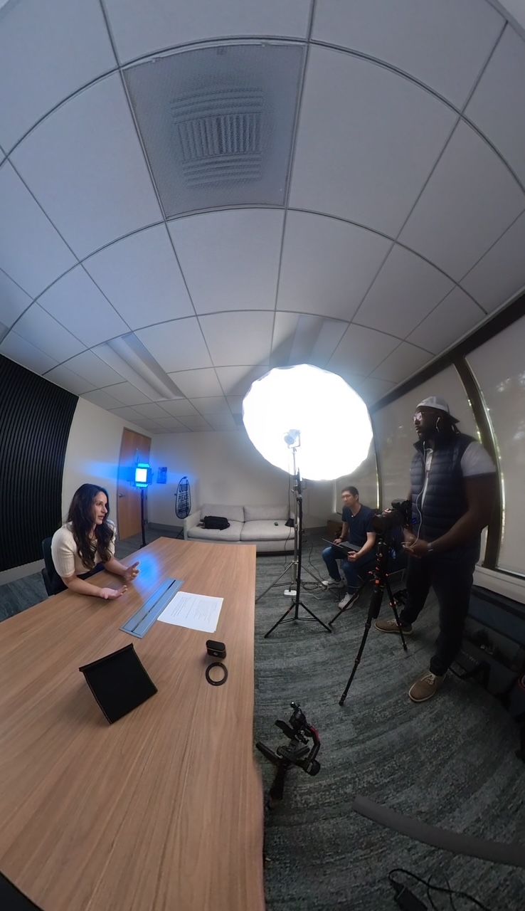 Professional video production setup in a modern office meeting room with studio lighting, camera equipment and curved fisheye perspective.