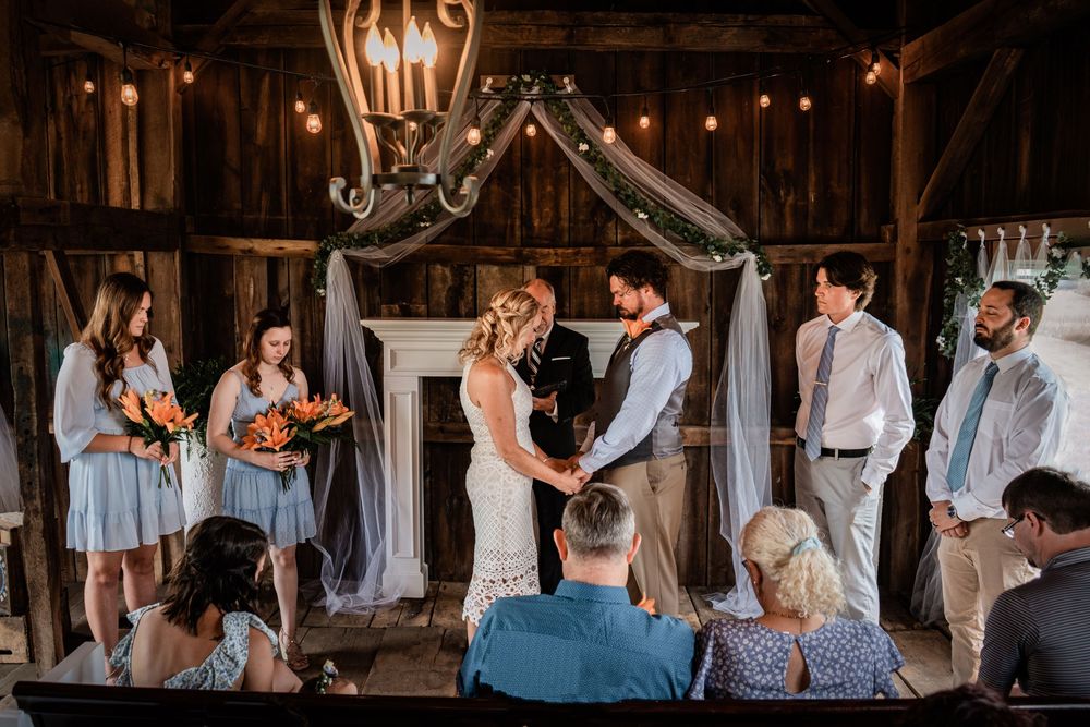 Rustic barn wedding ceremony with string lights and draped fabric decor.
