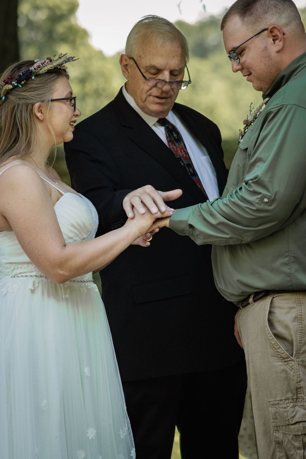 Wedding ceremony with couple exchanging rings under guidance of officiant in outdoor setting.