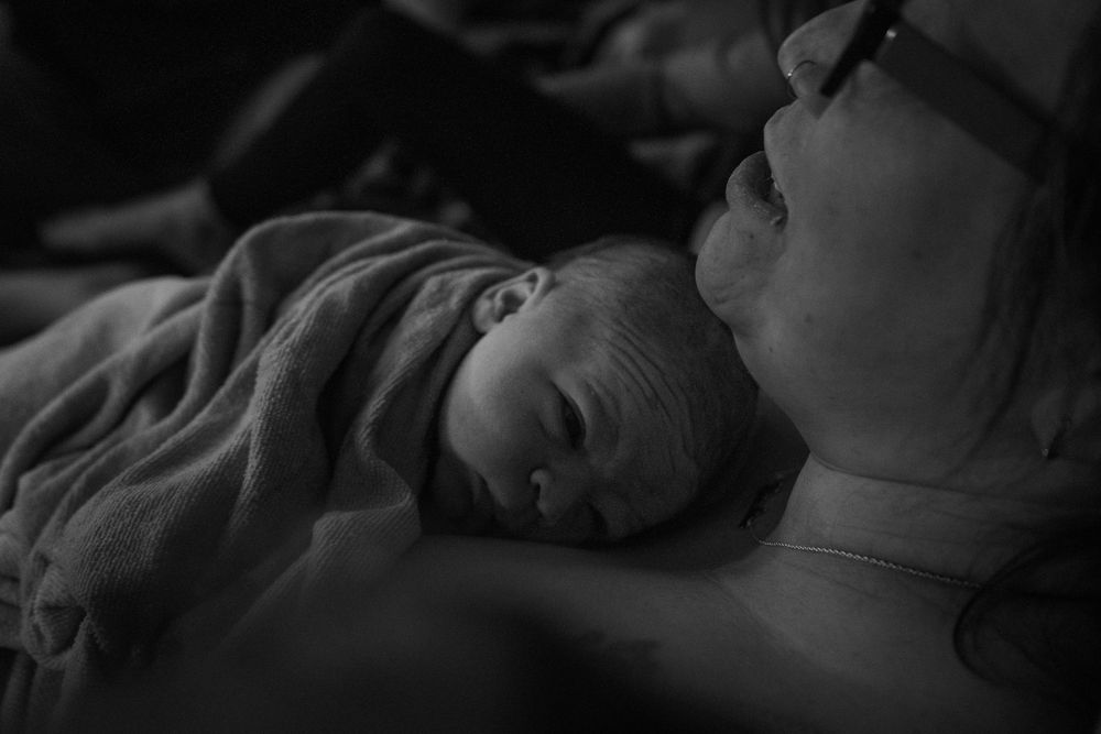 A tender black and white photograph of a newborn baby sleeping peacefully against someone in soft lighting.