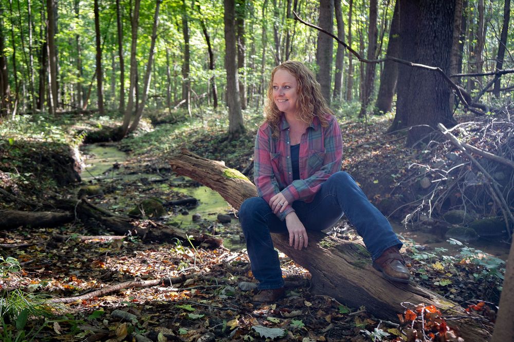 Person sitting on fallen log in autumn forest surrounded by leaves and moss.