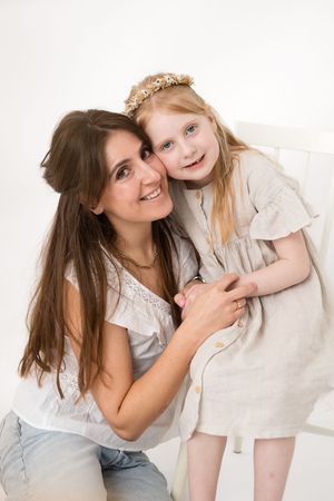 Two people embracing in white outfits share a joyful moment against a light background, creating a warm family portrait.