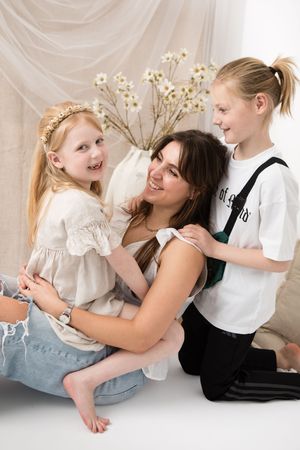 Three people sharing a joyful moment together against a light backdrop with floral decor.