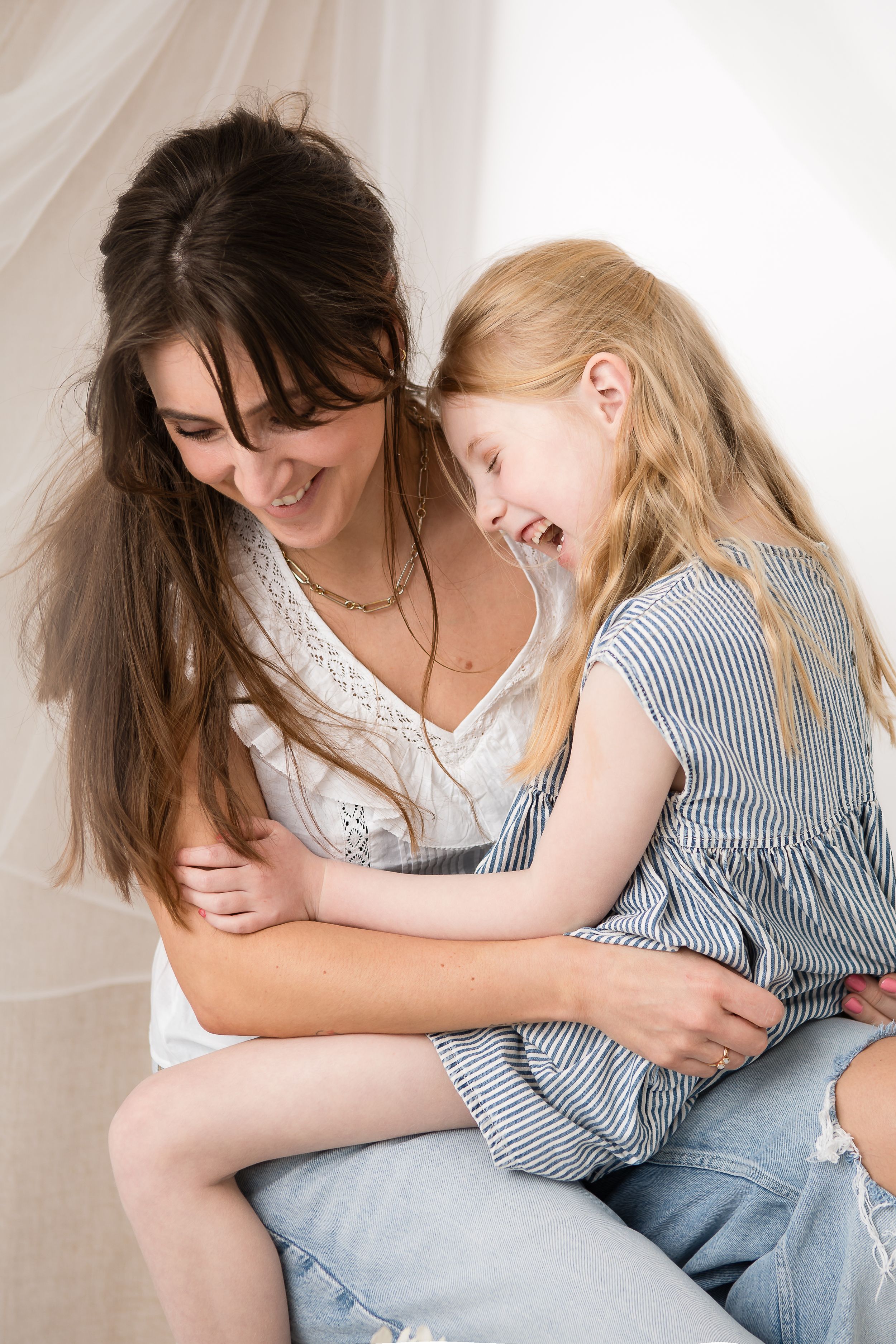 Two people share a candid laughing moment while sitting together against a neutral background.