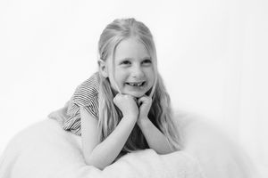 In a black and white portrait, a happy young subject with long hair rests on a white surface in a relaxed pose.