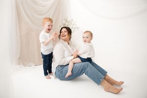 A casual family portrait with toddlers and adult wearing light colors against a white draped backdrop.