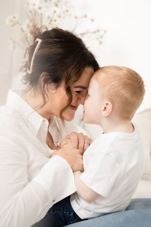 A tender moment shared between a parent and young child in white shirts as they touch noses and smile together.