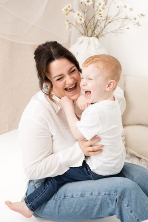 A joyful moment of laughter and cuddles shared between mother and young child on a couch with white decor.