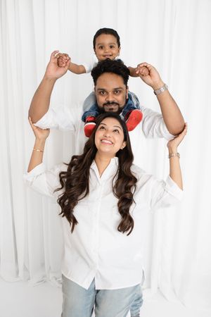 A happy family poses playfully together against a white backdrop wearing casual clothing.