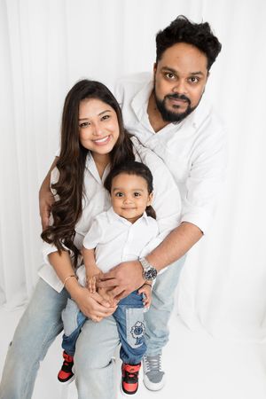 A family in matching white shirts and jeans poses together against a white backdrop for a casual portrait.
