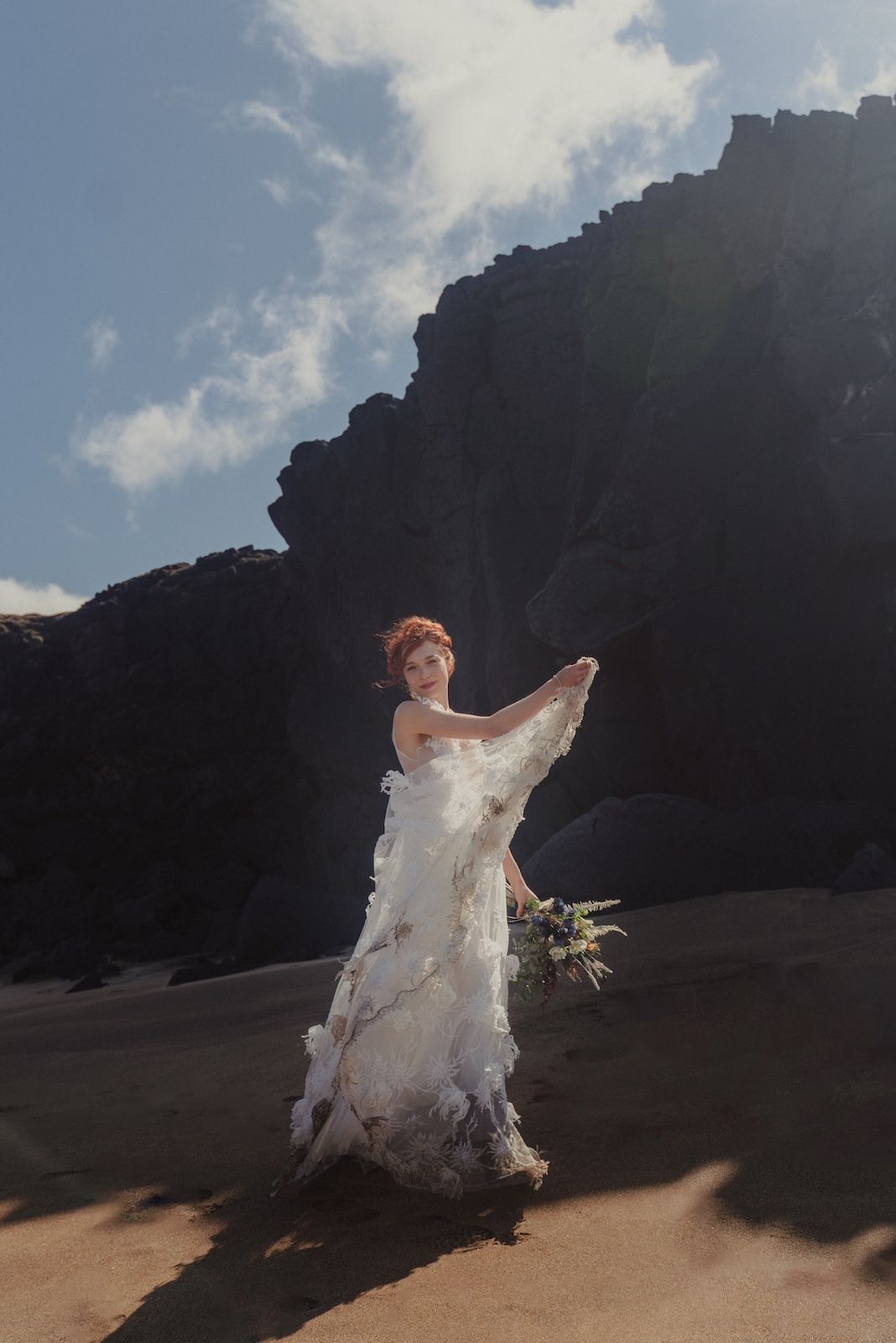 Bride dancing with her dress on a red sand beach.