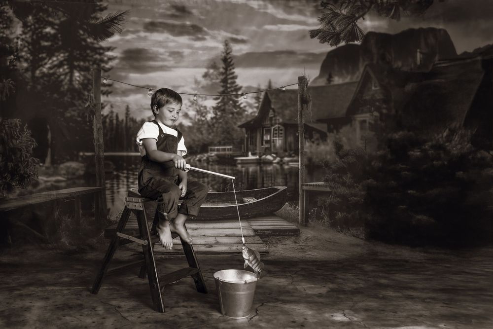 Vintage black and white photography showing a young child on a wooden chair washing clothes, set against a rustic outdoor scene.