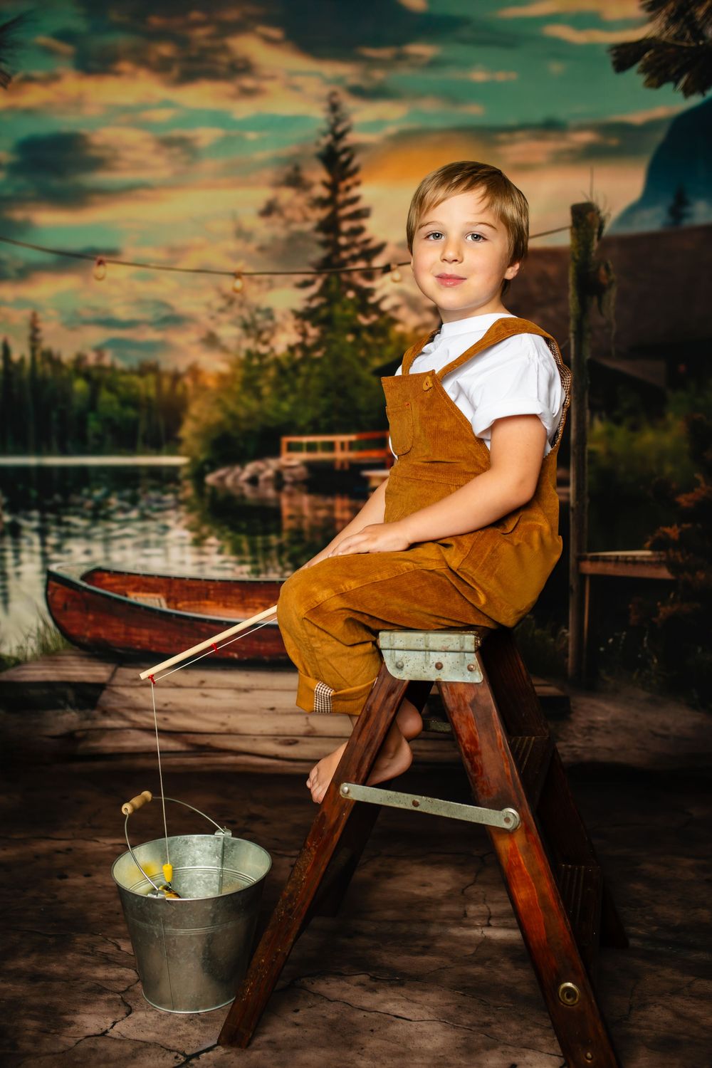 A child in brown overalls sits on a wooden ladder with fishing equipment at sunset by a serene lake.