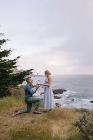 A romantic proposal takes place on a scenic coastal cliff overlooking the ocean at sunset.