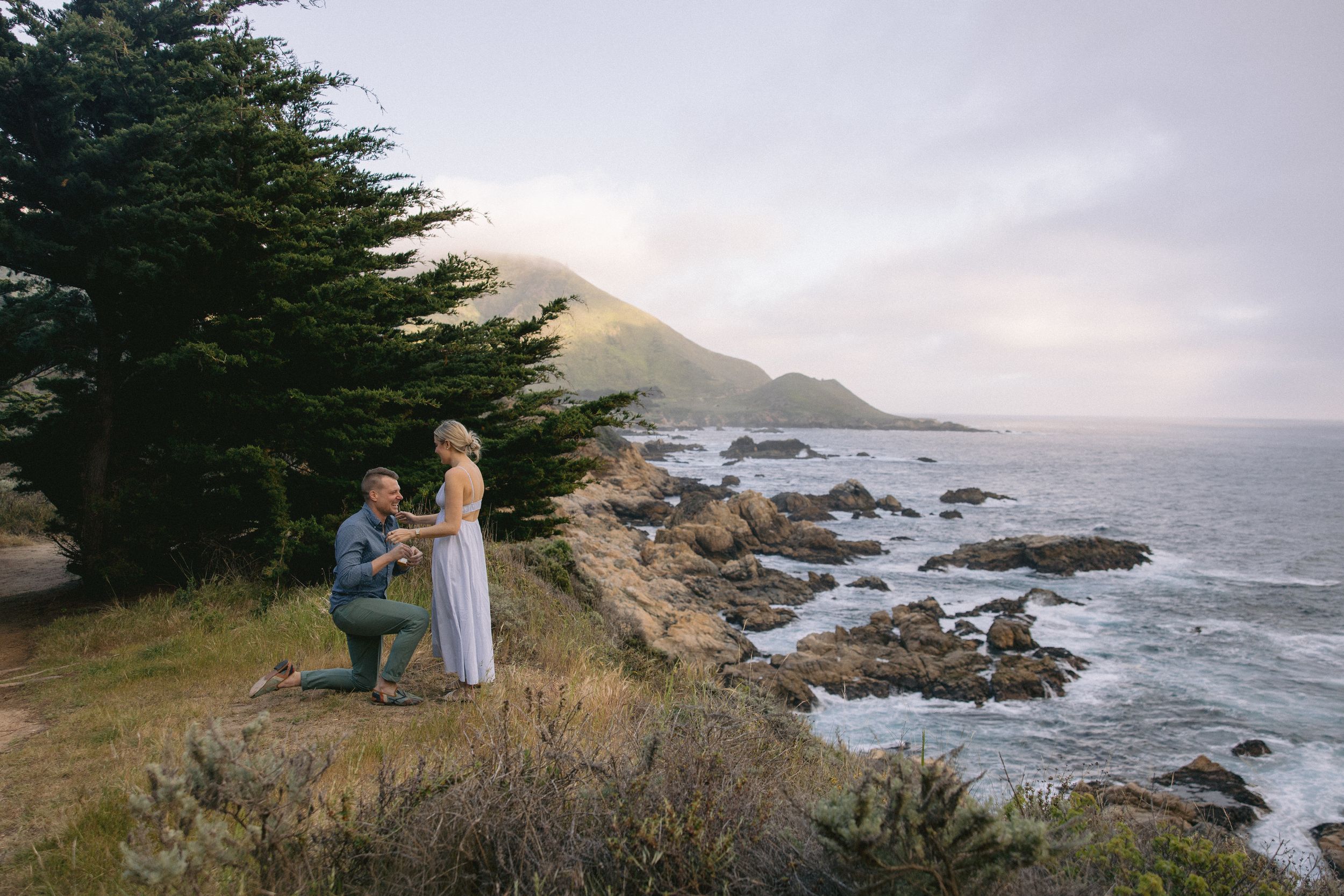 Special moment captured on scenic coastal bluff with mountain backdrop and rocky shoreline below.