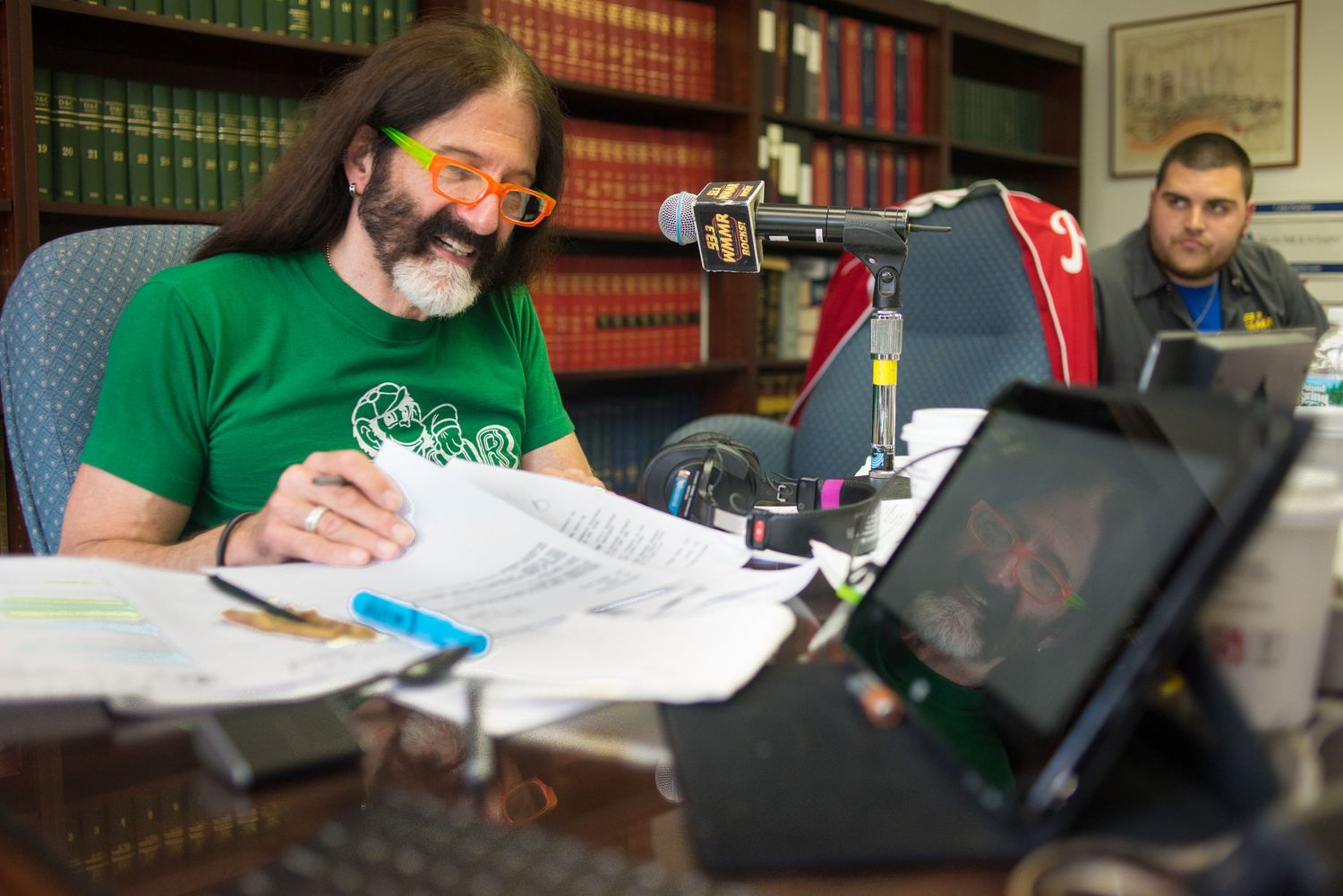 A person in a green shirt works at a desk surrounded by law books and computer screens.