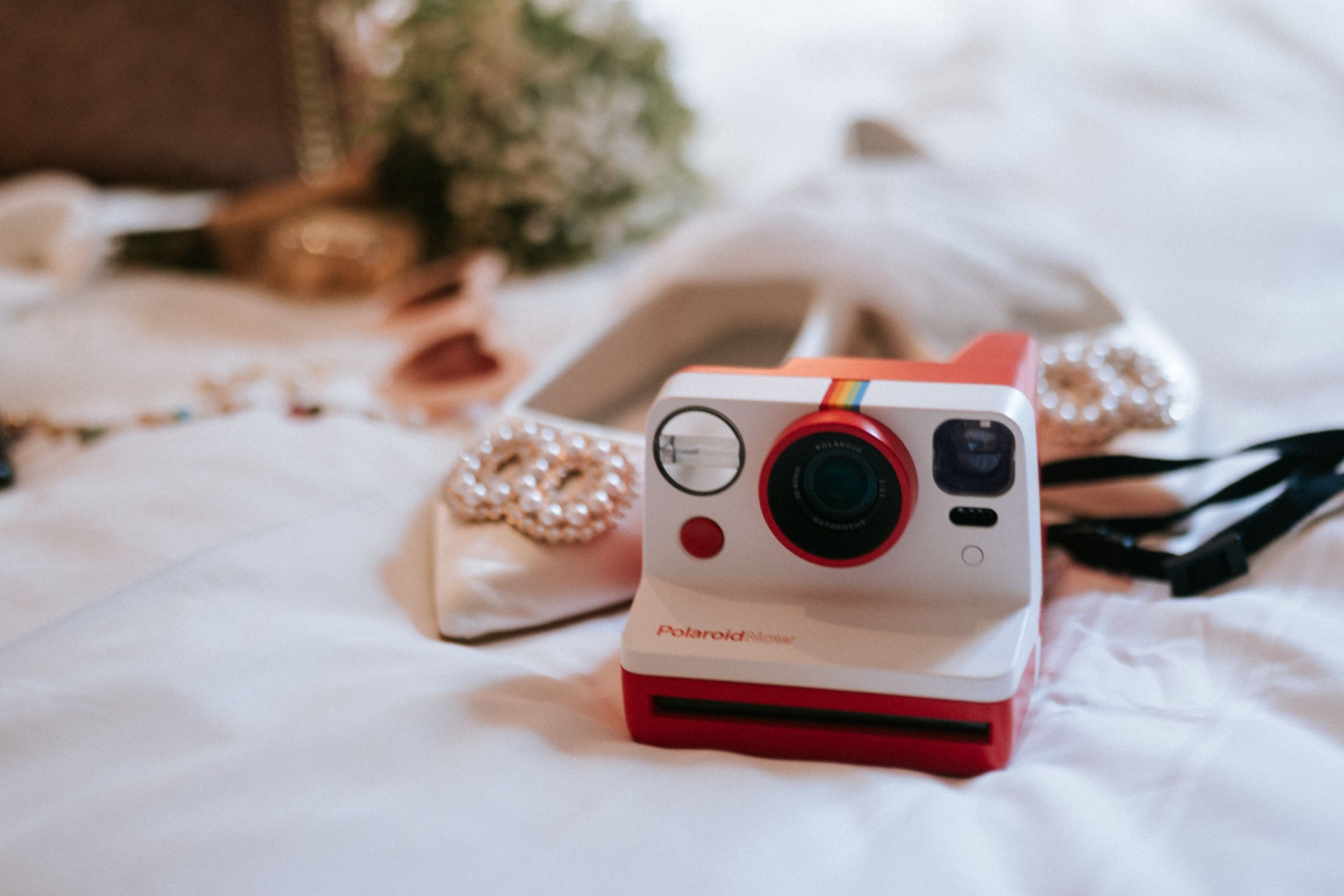 A retro-style white and red Polaroid camera sits on white fabric next to pastries in a dreamy composition.