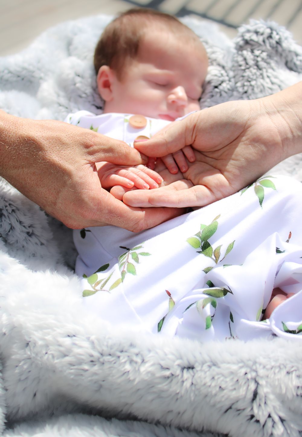 A tender moment showing adult hands gently holding a newborn baby's tiny hand on a floral patterned blanket.