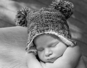 Peaceful sleeping baby wearing knit winter hat with pom poms in black and white portrait.