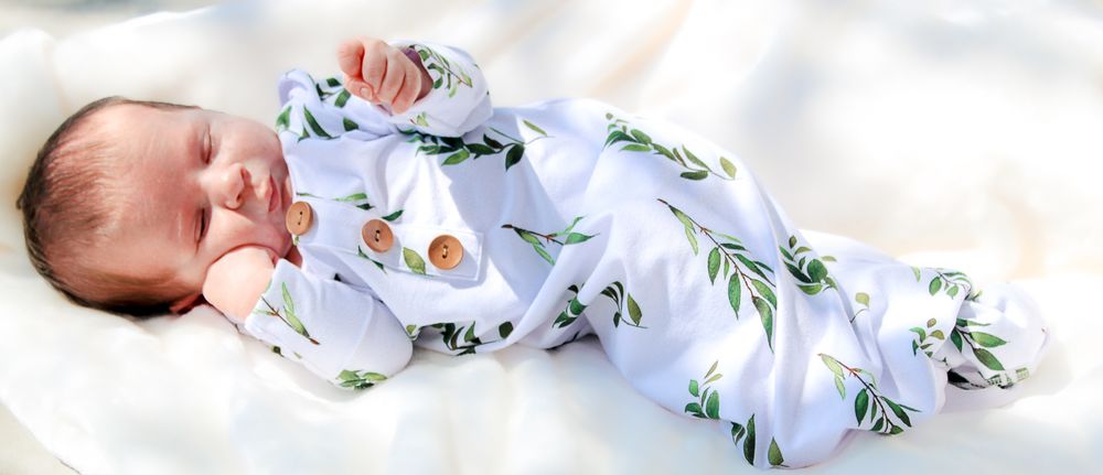 Sleeping baby wearing cozy blue and white floral printed footie pajamas rests on soft white bedding.