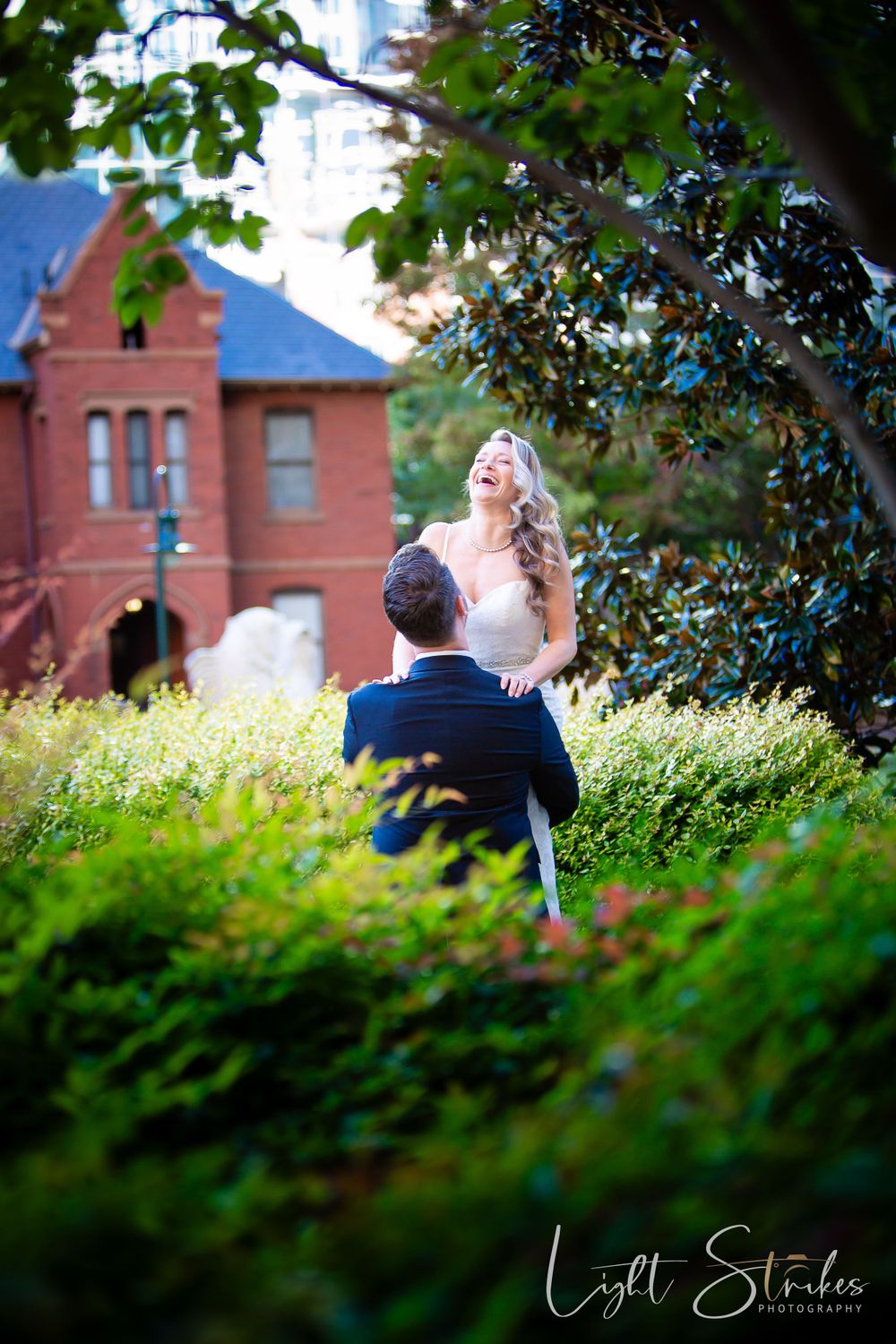 A romantic outdoor engagement photo with a couple embracing among lush green urban setting captured by wedding photographer in Charlotte.
