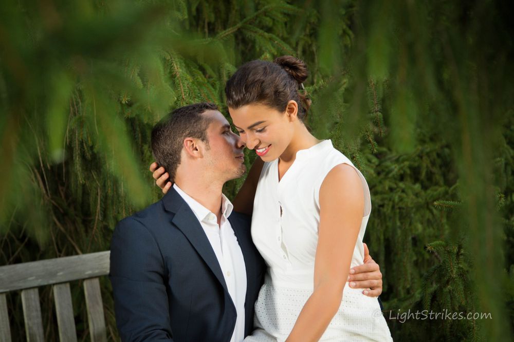 A tender moment between two people sharing an intimate laugh while sitting on a bench in a lush garden setting during engagement session.