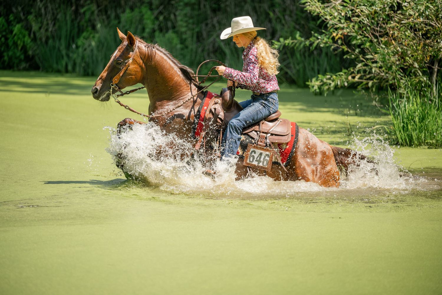 Horse and rider splashing through water during western riding event.