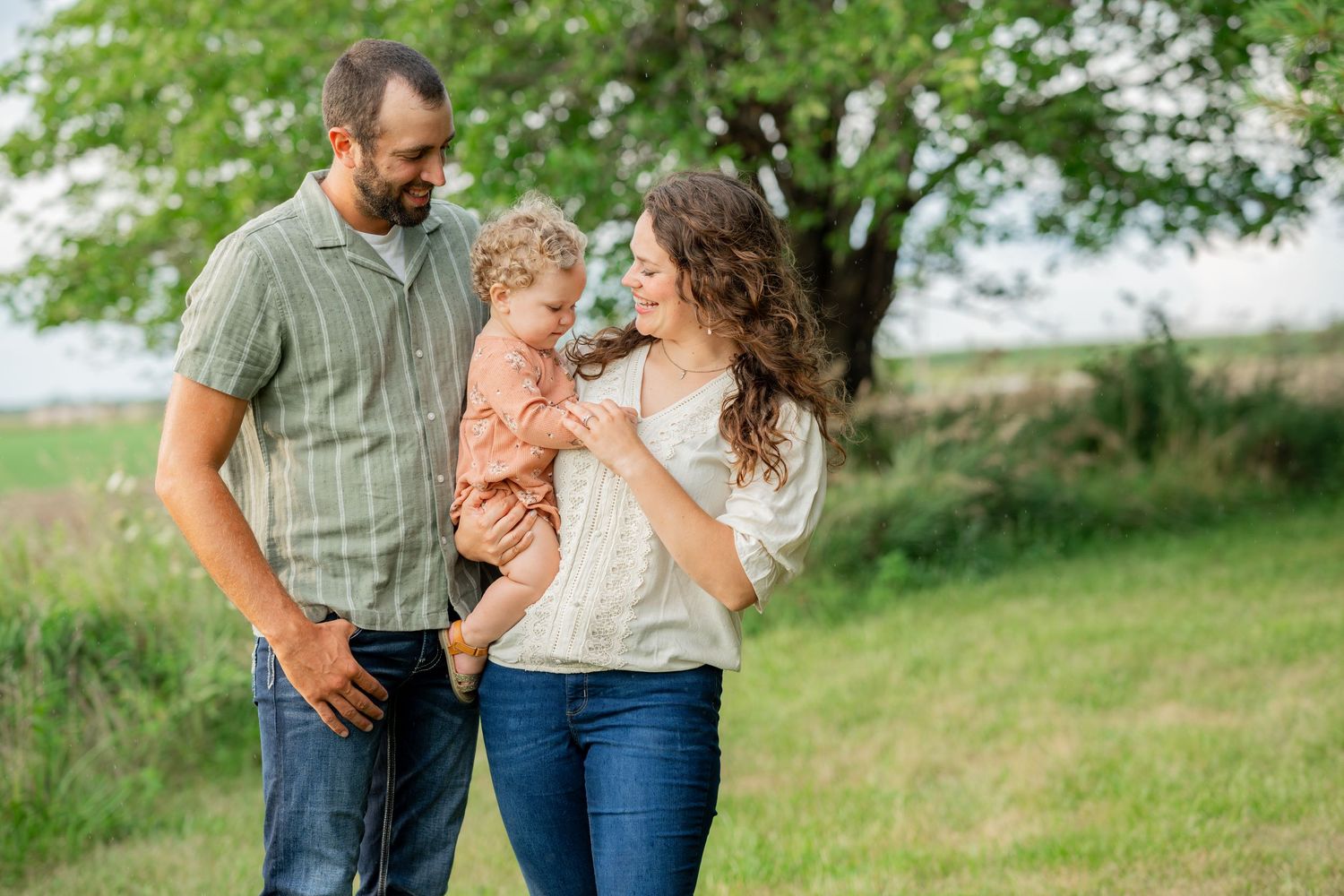 Family enjoying a tender moment together in a sunny field with green trees.