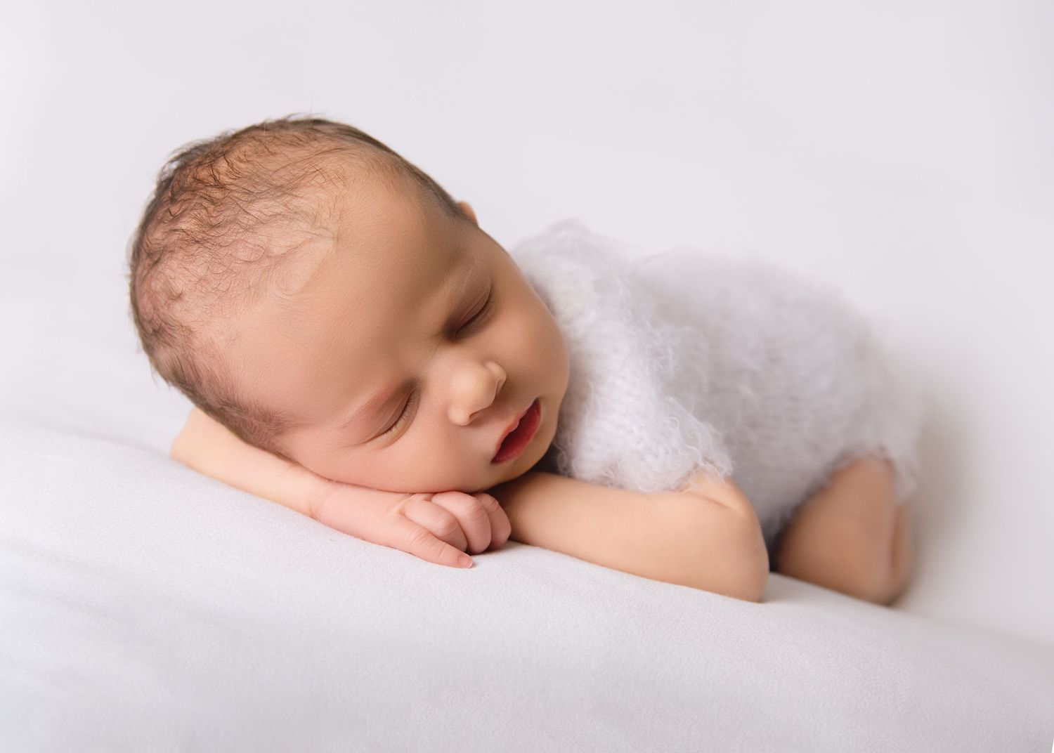 Baby asleep on arms curled up.