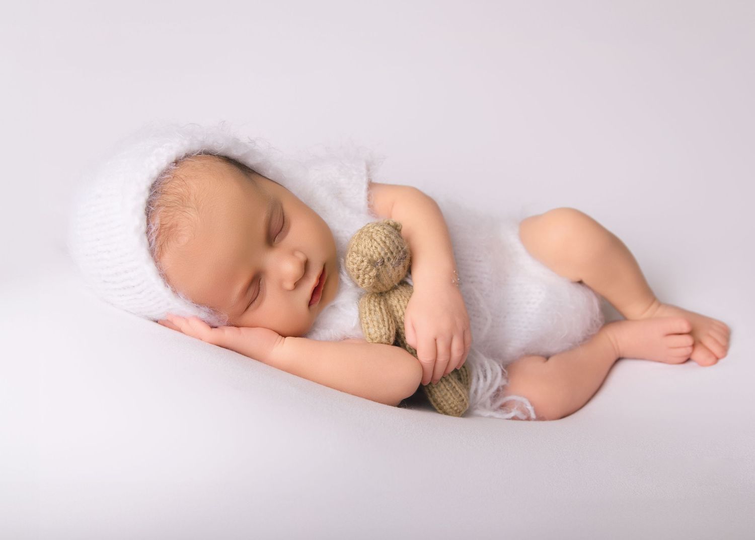 Baby asleep with bear wearing fluffy bonnet.