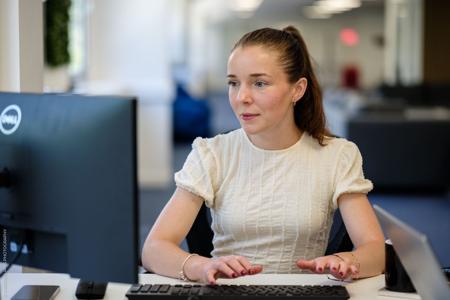 Young woman in white top working at a Dell computer in a modern office environment.