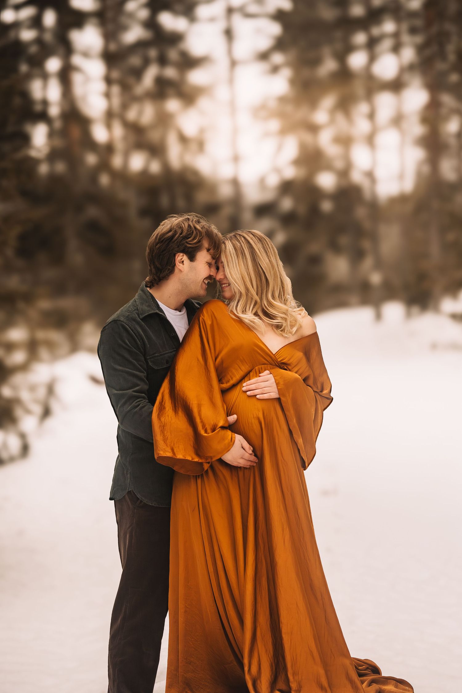 Maternity portrait of a woman in a flowing rust-colored dress standing in an autumn forest.