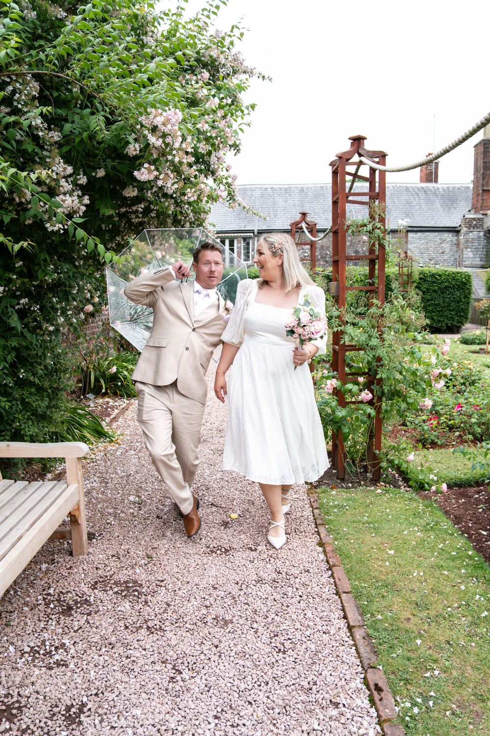 A couple walks together on a garden path surrounded by blooming flowers and greenery on their wedding day.