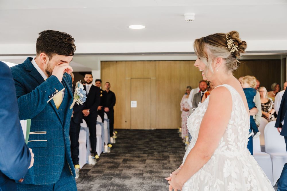 Emotional groom wipes tears as bride walks down the aisle during wedding ceremony.