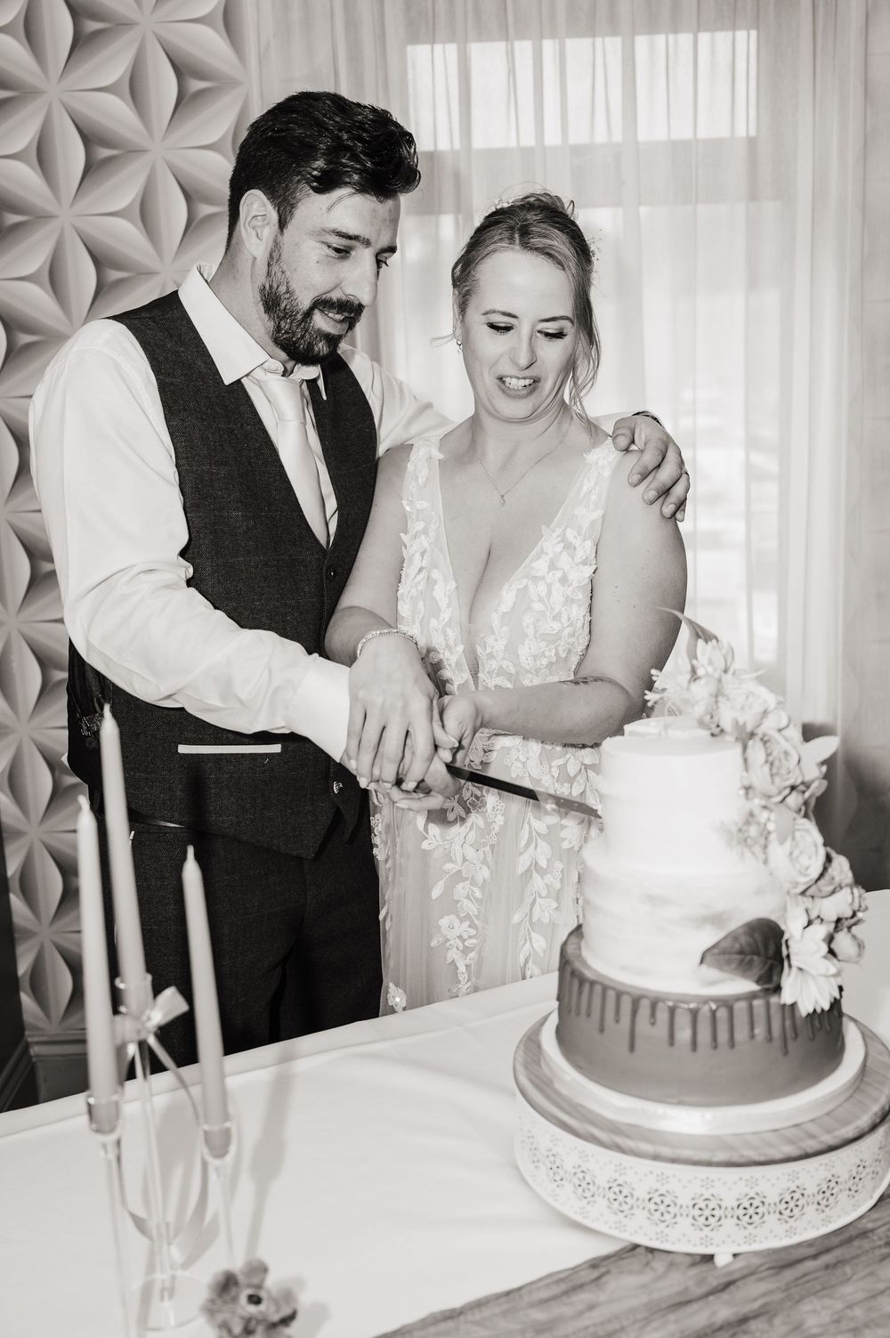 Bride and groom cut tiered wedding cake together in classic black and white reception photo.