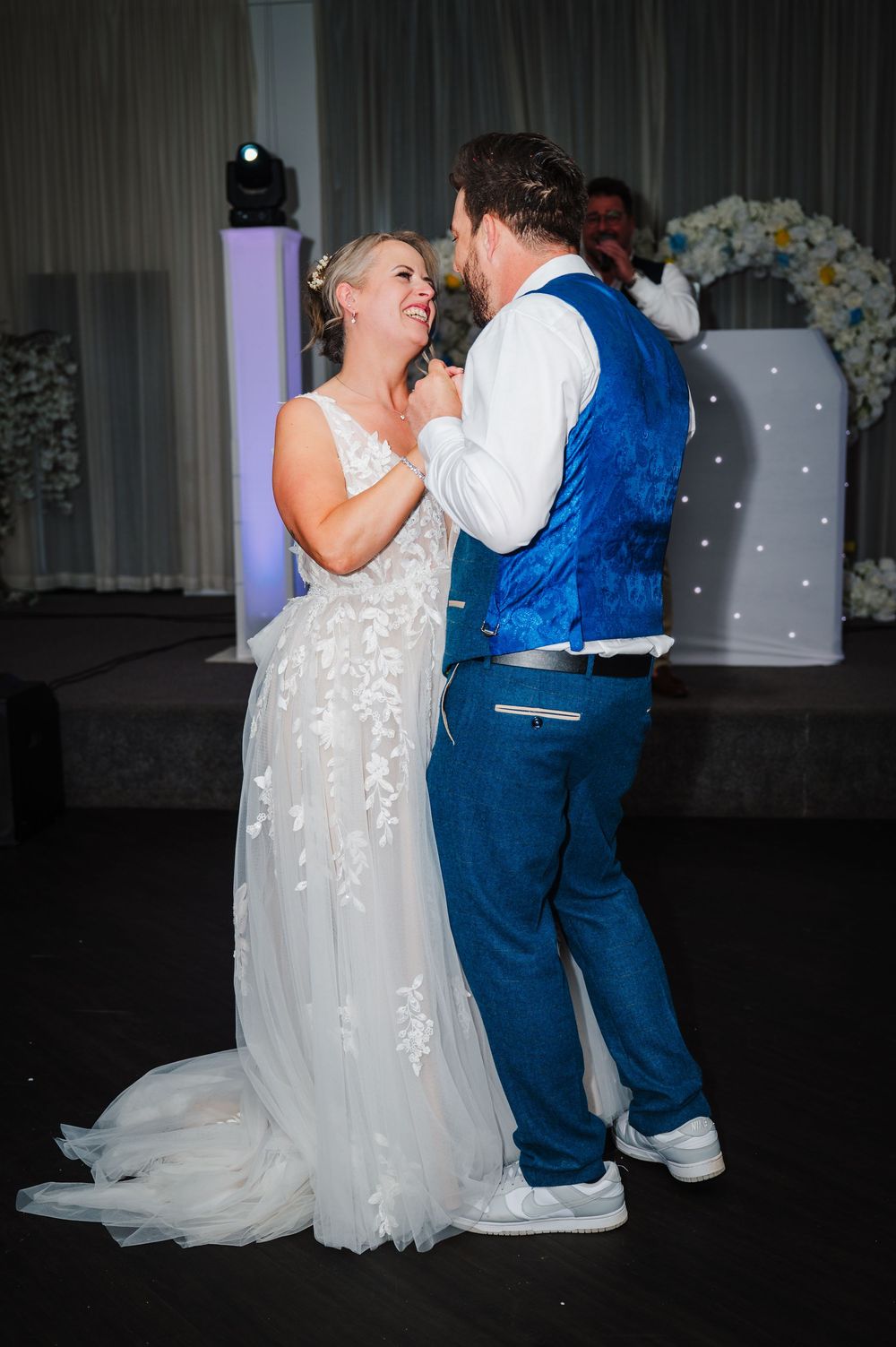 Bride and groom share joyful first dance at wedding reception with floral backdrop.