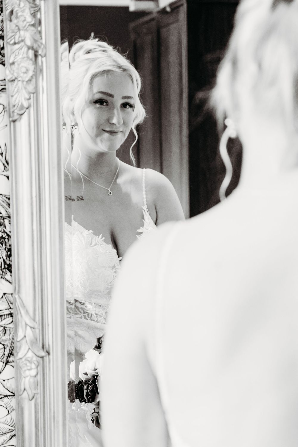 Black and white wedding photo showing a bride reflected in elegant framed mirrors.
