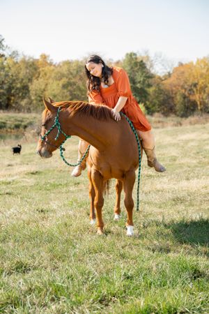 A person in an orange dress rides bareback on a chestnut horse through an autumn field.